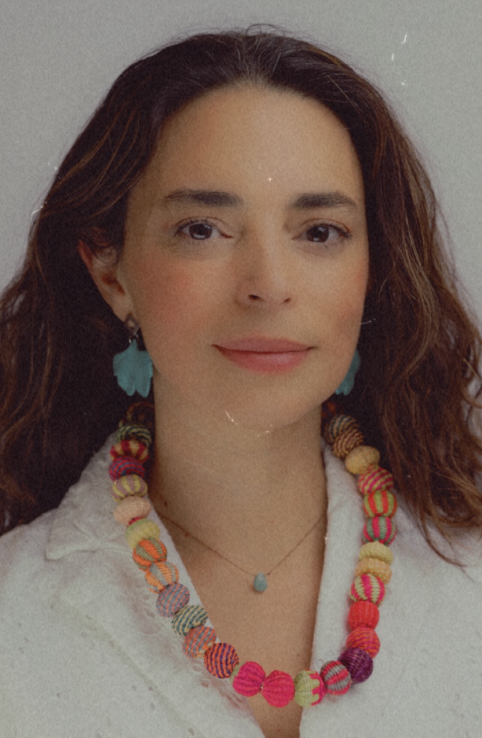 Uri Ramos headshot - fair-skinned woman with long brown hair wearing white shirt and colorfol necklace