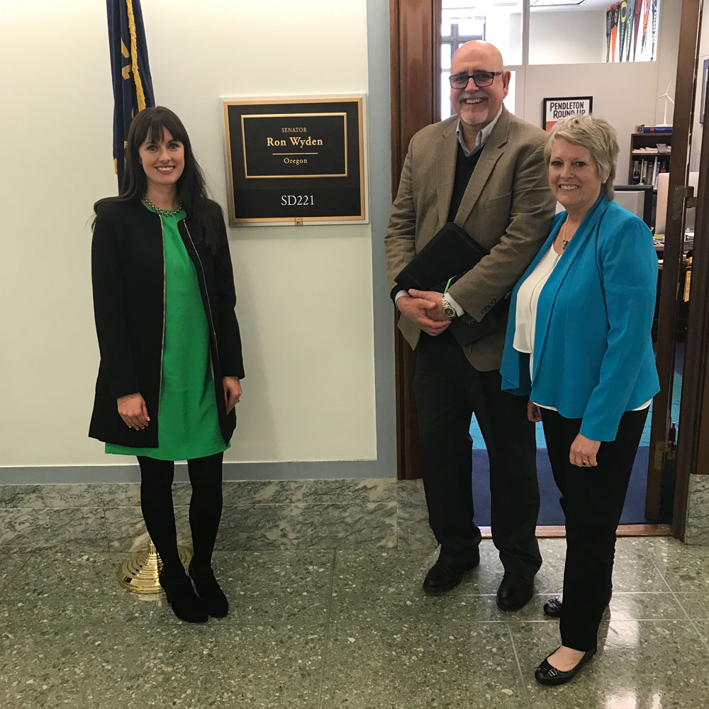 Team Oregon Three people stand in front of hallway plaque