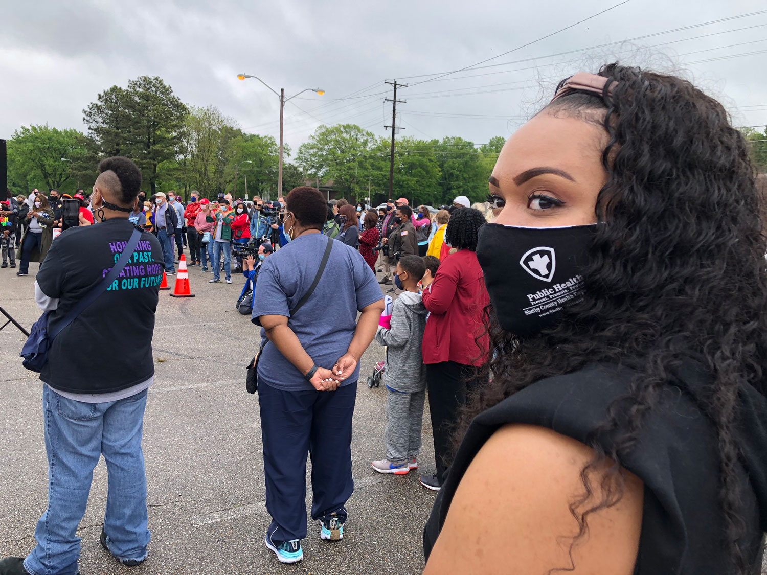 Team Shelby People on street, masked person looks over shoulder at camera