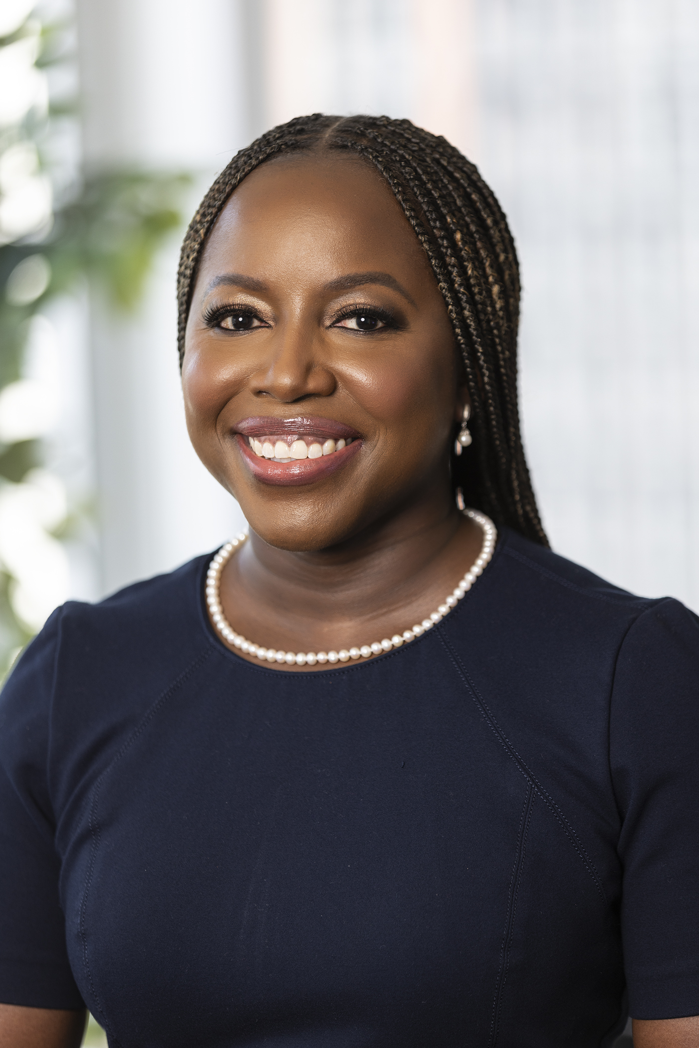 Professional headshot of a black woman with braids who is wearing a navy blue dress and smiling.