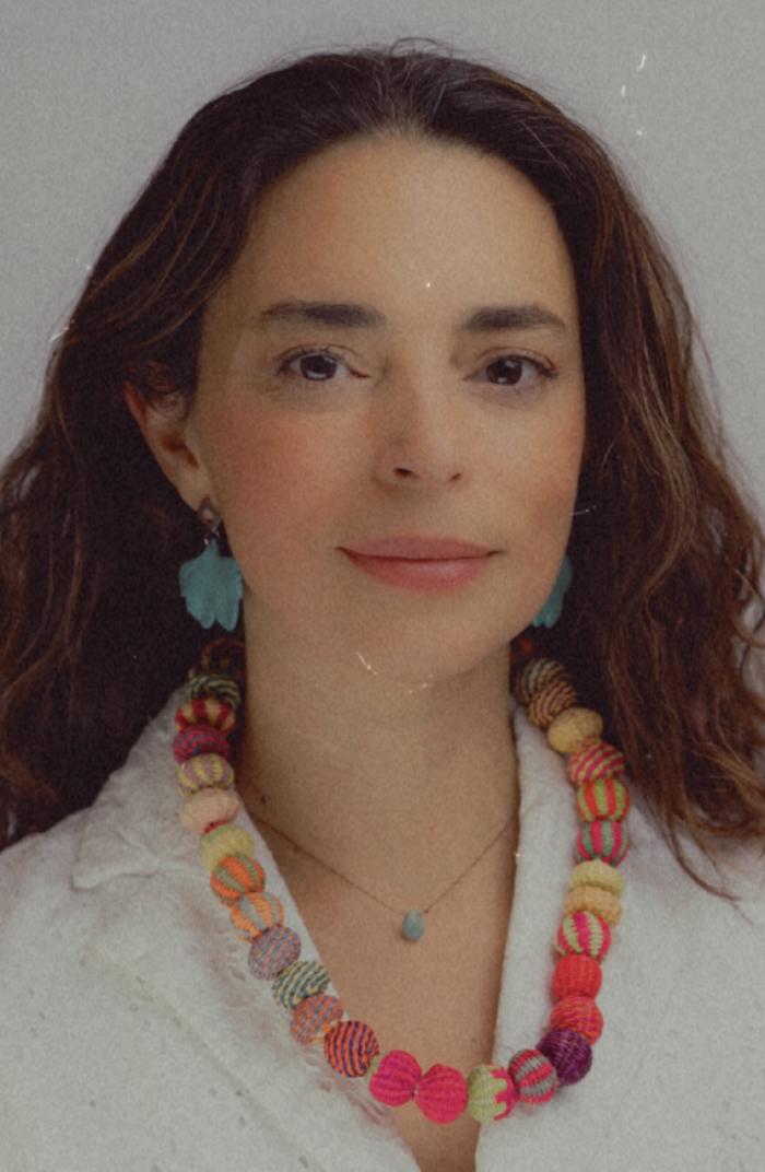 Uri Ramos headshot - fair-skinned woman with long brown hair wearing white shirt and colorfol necklace