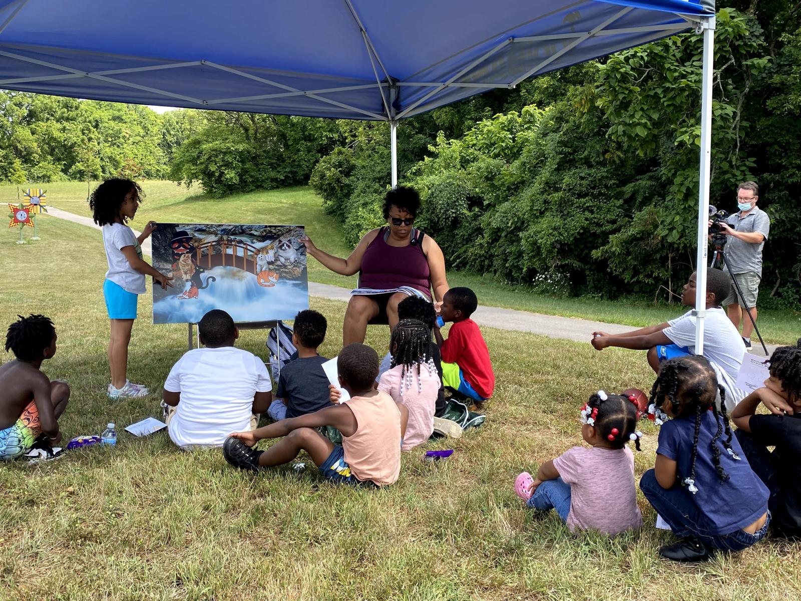 African American person reads a book to children in a park